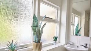 Ein Badezimmer mit Fenster, Waschbecken und drei Blumentöpfen.