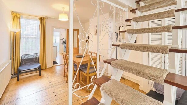 Eine Treppe mit einer Katzenklappe, Holzböden und einem Essbereich mit Stühlen und einem Tisch.