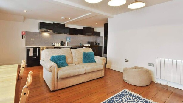 En moderne stue med en beige sofa, et blåt tæppe med mønster og trægulv.