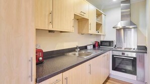 A modern kitchen with light wood cabinets, a stainless steel range hood, a microwave, and a built-in oven.