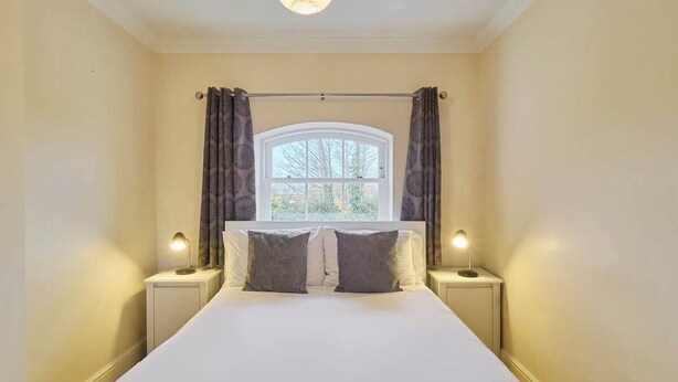 A neatly made bed with two pillows, a window with curtains, and bedside lamps.