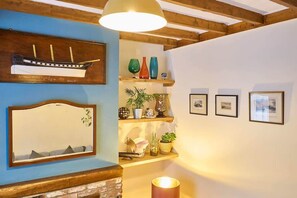 Quarto com teto de madeira, espelho, prateleira com objetos decorativos e quadros na parede.