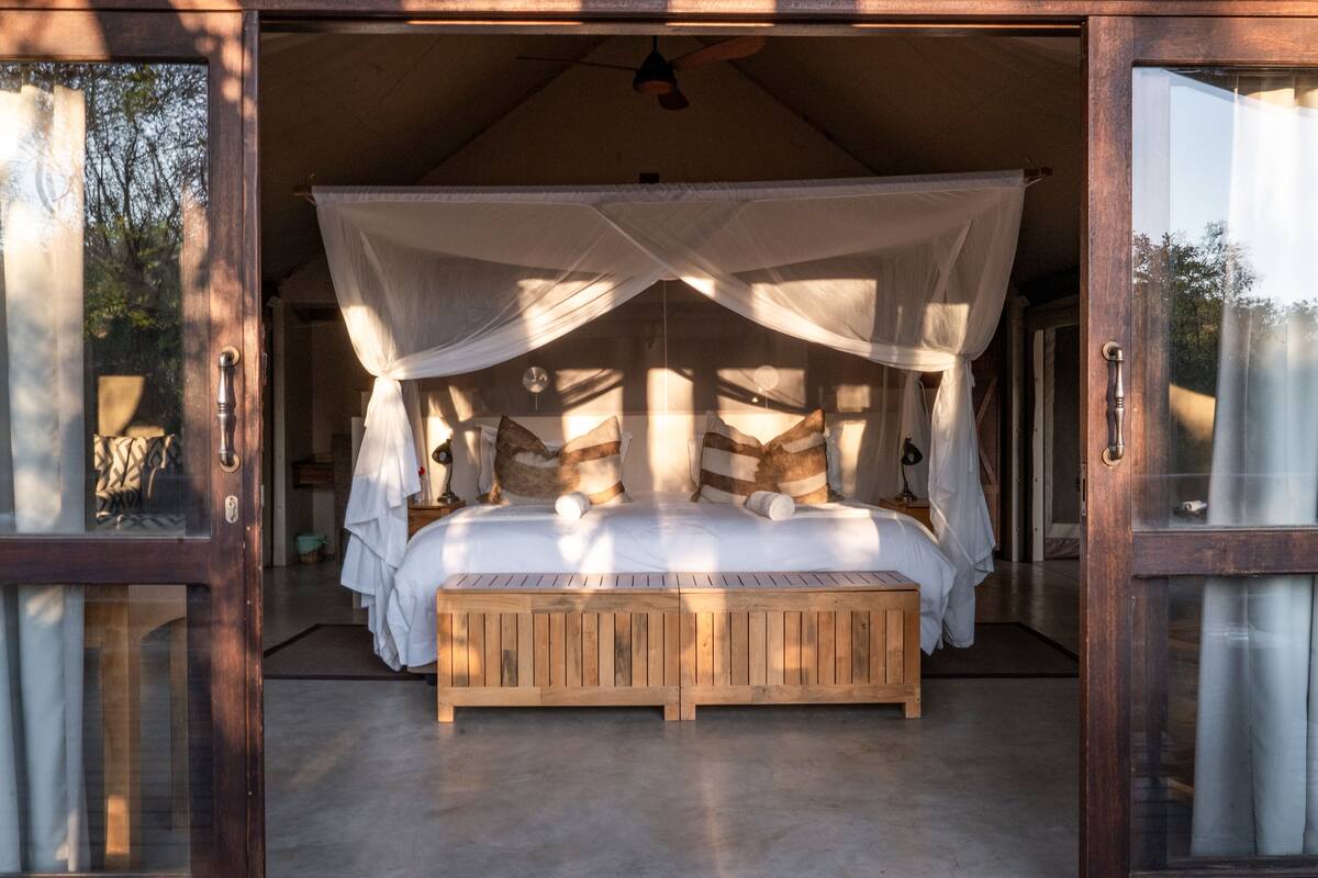 A wooden four-poster bed with a canopy, a wooden bench, and a bedside table with a lamp.