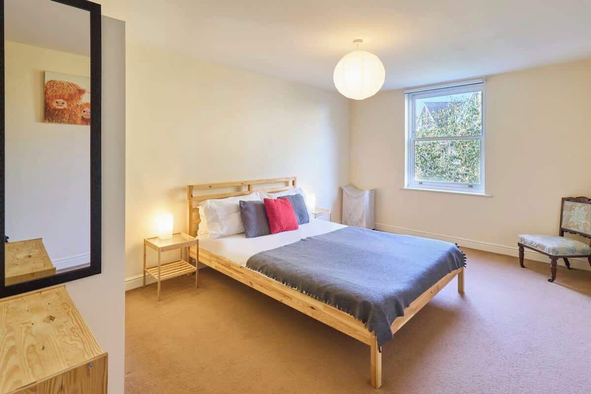 A bedroom with a wooden bed, bedside tables, a mirror, a window with a view of greenery, and a chair.