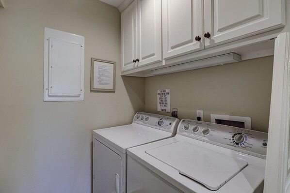 A laundry room with two white washers and dryers, a vent sign, and a door with a lock. - Sunset Rentals | Racquet Club 2358 | Dog-Friendly (Hilton Head Island)