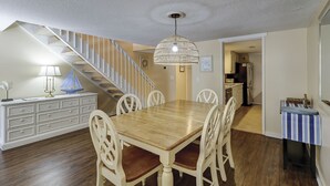Un coin repas avec une table et des chaises en bois, un lustre et un escalier menant à une autre pièce.