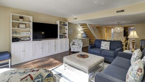 Un salon avec une télévision, un canapé et une table basse. Un escalier mène à un autre niveau.