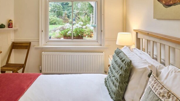 Ein Schlafzimmer mit Bett, einem Fenster mit Gartenblick, einer Heizung und einem Holzstuhl.