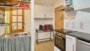 Eine kompakte Küche mit Spüle, Herd, Backofen und Geschirrspüler. Ein kleiner Tisch mit Wasserkocher und einer roten Mikrowelle.