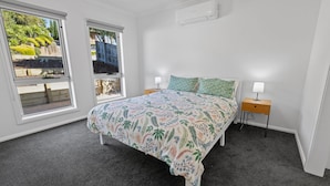 Une chambre à coucher comprenant un lit, deux tables de chevet, une fenêtre et un appareil de climatisation.