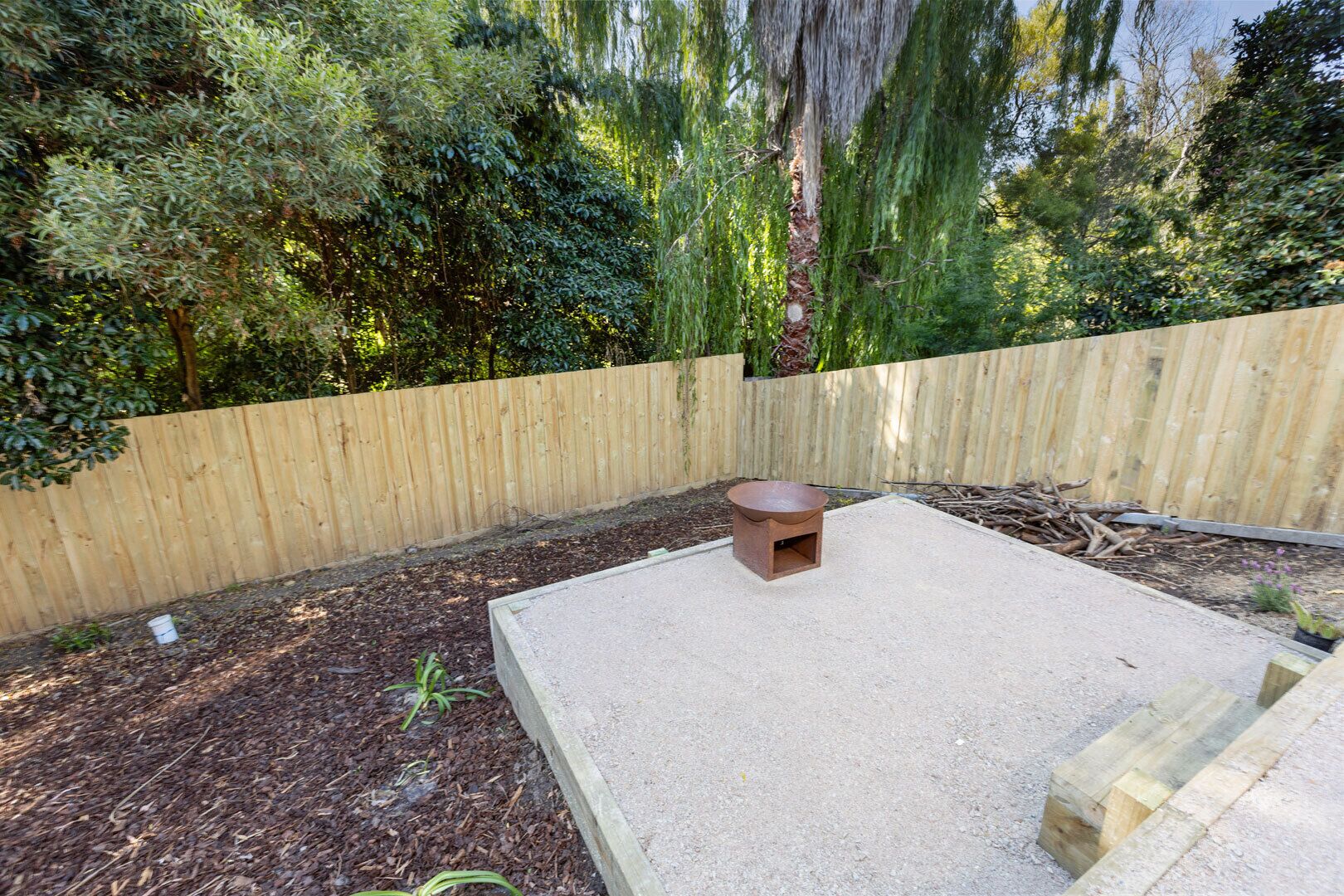 A backyard with a concrete patio, a small fire pit, and a wooden fence.