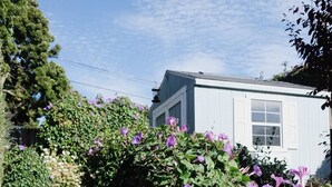 Ein Haus mit einer hölzernen Treppe, die zu einer Tür führt, umgeben von lila Blumen und Grünpflanzen.