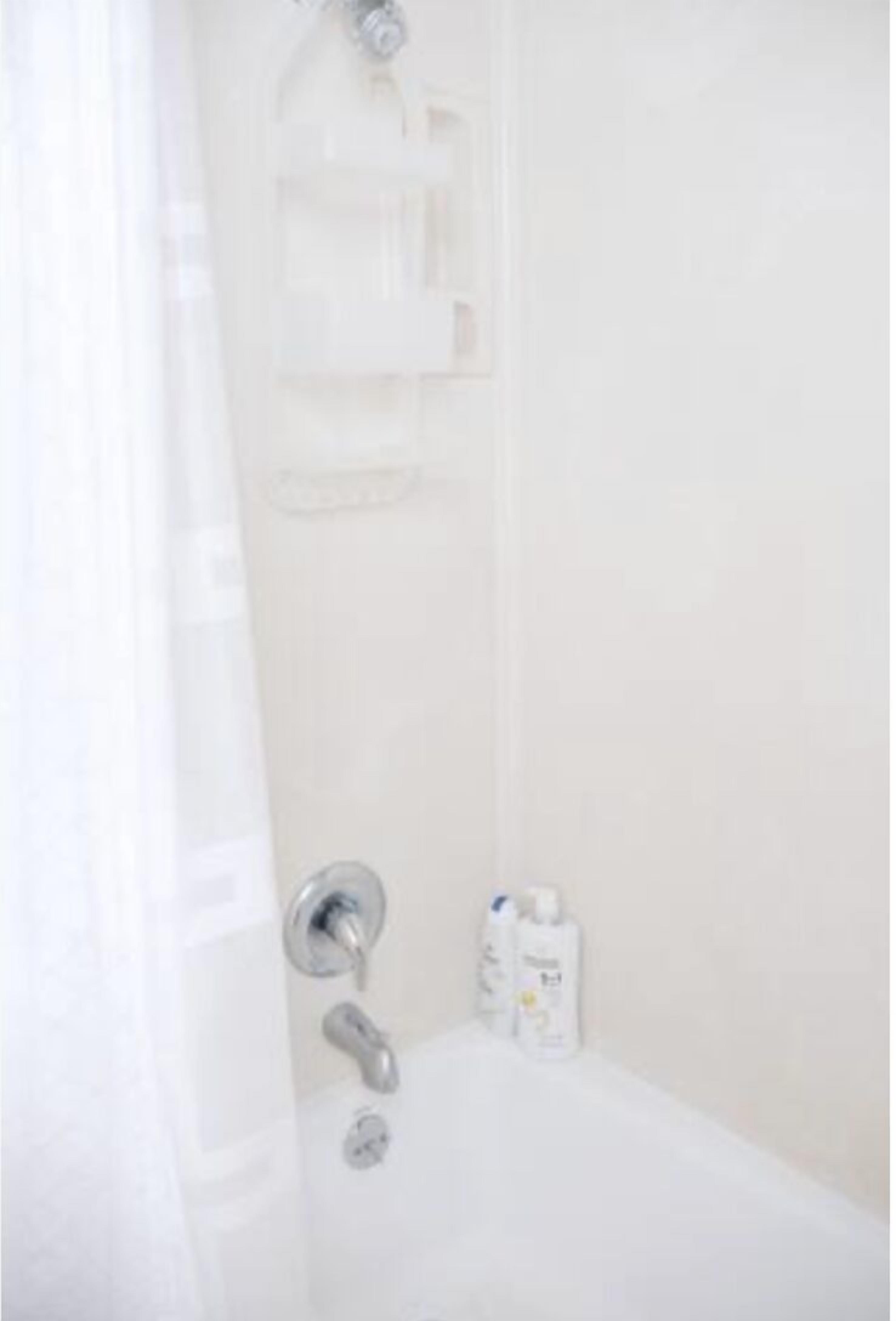 A bathroom with a bathtub, a shower, and a toilet. There are toiletries on the side of the tub.