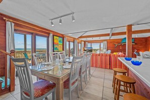 A dining area with a view of the beach, wooden walls, and a large painting.