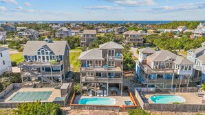 Une propriété située en bord de mer, comprenant plusieurs maisons à deux étages, chacune dotée d’un balcon et d’une petite piscine.