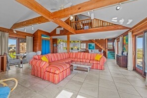 A spacious living area with a large sectional sofa, a dining table with chairs, and a kitchen in the background.
