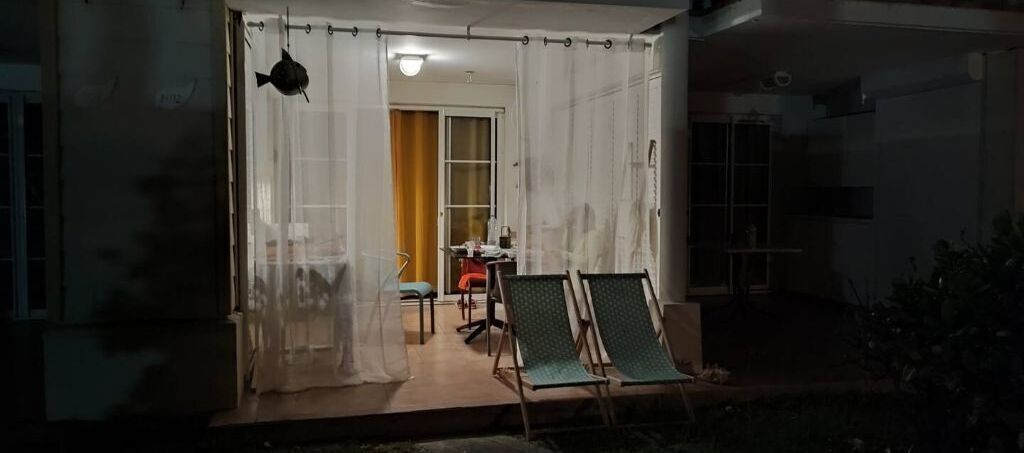 A covered outdoor area with two green lounge chairs, a table, and a chair.
