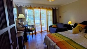 A hotel room with a bed, a desk, a chair, and a view through a window. - Studio vue mer Gwada ds Village Vacances Ste Anne (Sainte-Anne)