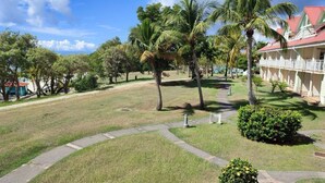 A hotel with a red roof, surrounded by palm trees and a well-maintained lawn. - Studio vue mer Gwada ds Village Vacances Ste Anne (Sainte-Anne)