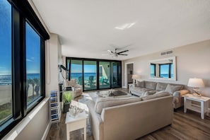 A spacious living room with a large window overlooking the ocean, a ceiling fan, and a comfortable seating area.