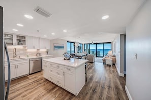 A modern kitchen with white cabinetry, a central island, and a dining area with a view.