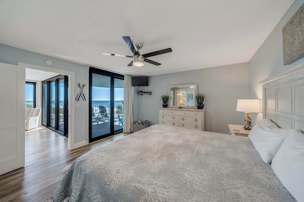 A bedroom with a bed, a dresser, a ceiling fan, and a view of the outdoors.