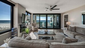 A spacious living room with a large window overlooking the beach, a ceiling fan, and a comfortable seating area. - Watercrest 302 Amazing VIEW, Pool, Hot Tub, Tennis, Gym, FREE Golf & Perks! (Panama City Beach)