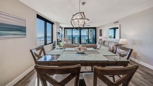 A dining area with a glass table, wooden chairs, and a chandelier. - Watercrest 302 Amazing VIEW, Pool, Hot Tub, Tennis, Gym, FREE Golf & Perks! (Panama City Beach)