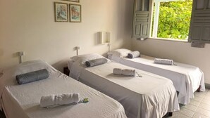 A hotel room with two single beds, a window with shutters, a wall-mounted air conditioning unit, and framed pictures. - Pousada Tropicália Tranquilid. Beira Mar (Santa Cruz Cabralia)