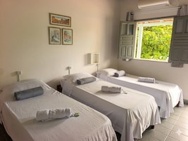 Habitación de hotel con dos camas individuales, una ventana con contraventanas, un aire acondicionado de pared y cuadros enmarcados.