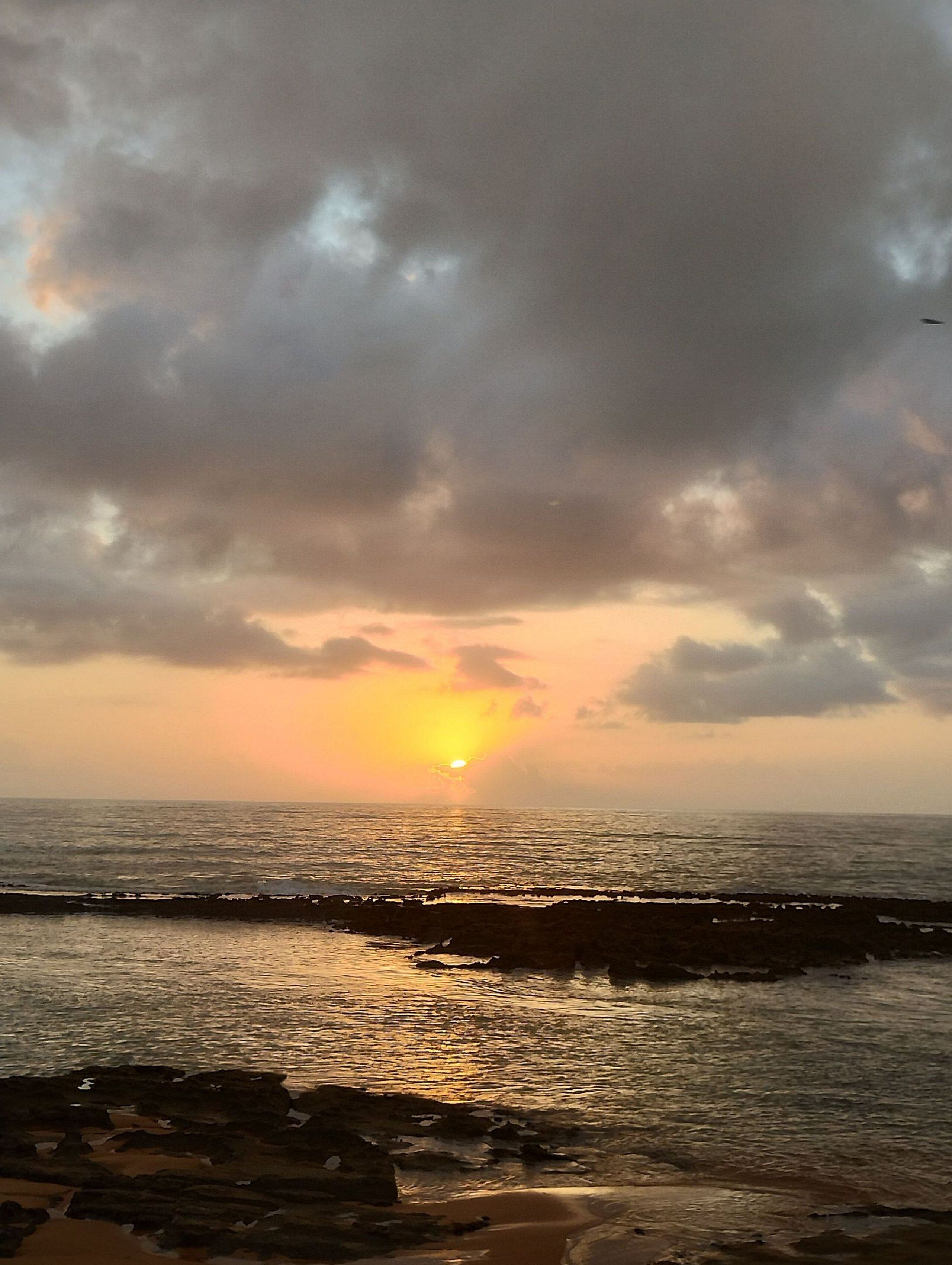 A sunset over a body of water with a rocky shoreline.