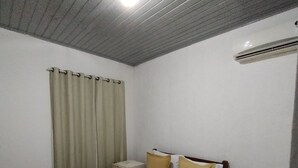 Un dormitorio con cama, mesita de noche, banco y luz de techo.