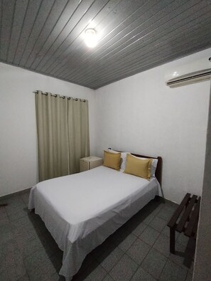 Un dormitorio con cama, mesita de noche, banco y luz de techo.