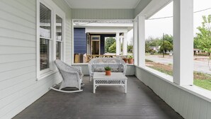 Eine Veranda mit weißen Geländern, einem Schaukelstuhl, einem Tisch mit einer Topfpflanze und einer hängenden Leuchte.