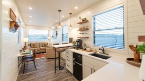 Une cuisine moderne avec des meubles blancs, un coin repas doté d’une table et de chaises blanches, et une vue sur l’extérieur grâce à de grandes fenêtres.