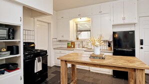 A modern kitchen with white cabinetry, a black stove, and a wooden table.