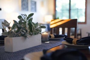 A dining table with a candle, a potted plant, and neatly folded napkins.