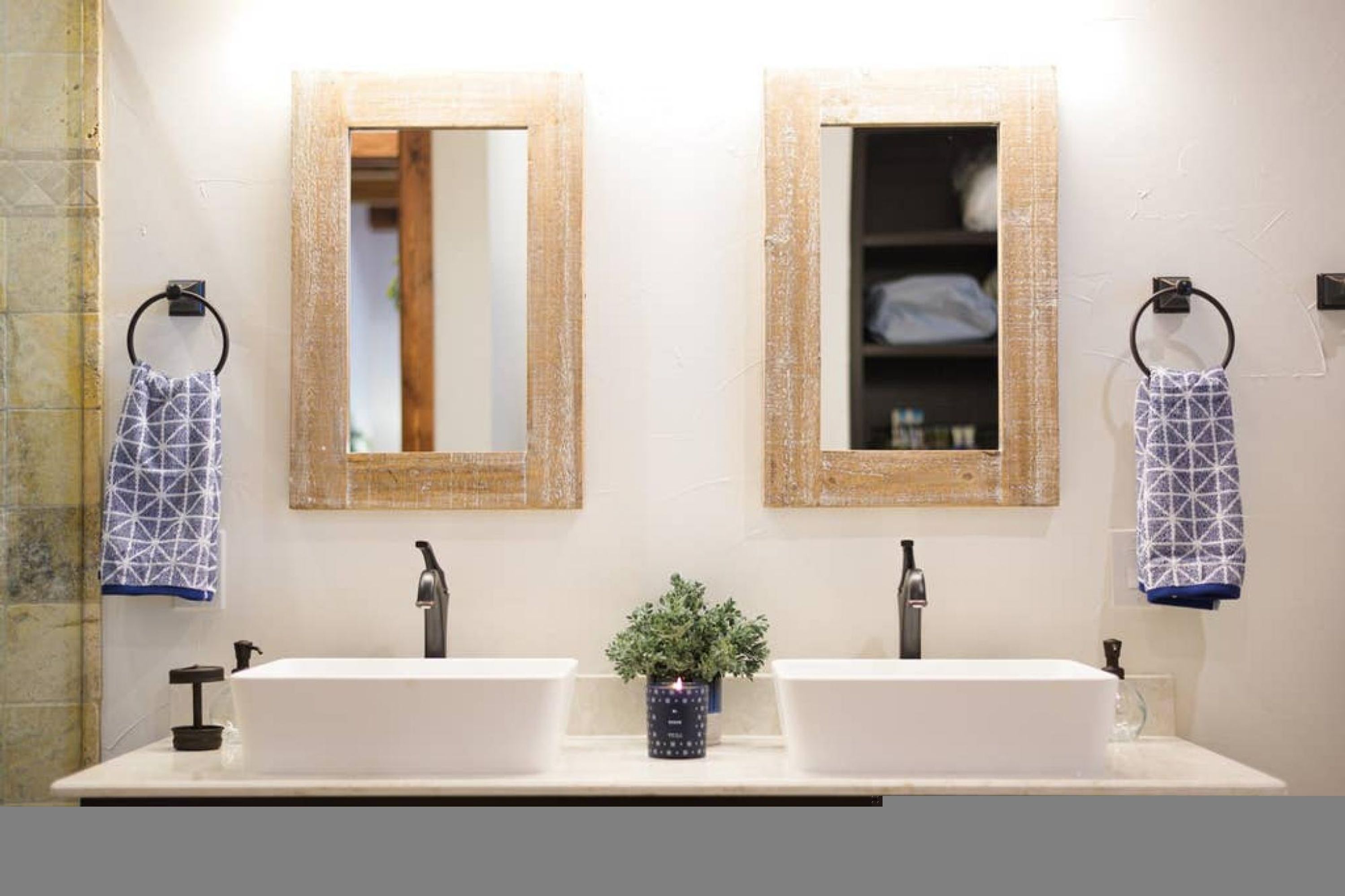 A bathroom with two sinks, a potted plant, and wooden-framed mirrors.