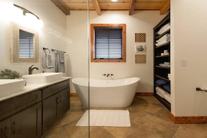 A modern bathroom with a freestanding bathtub, a double sink vanity, and a window with blinds.