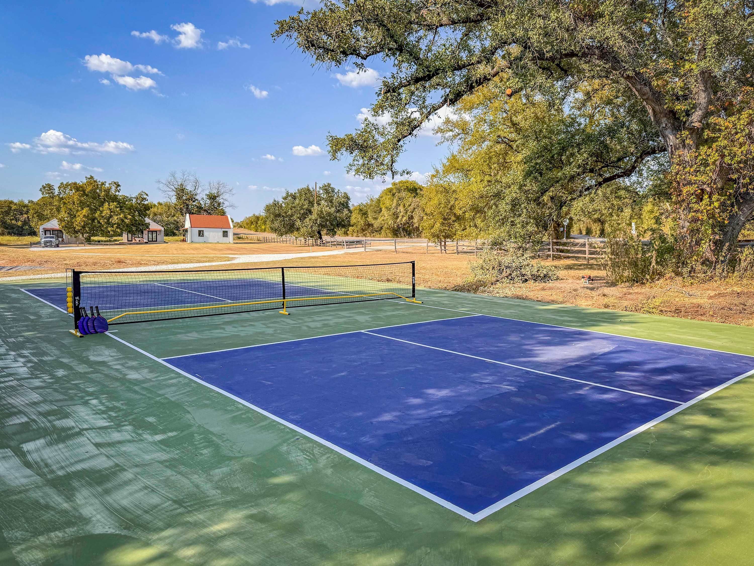 Een tennisbaan met net, omgeven door bomen en een hek.