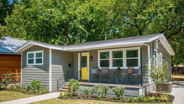 Ein eingeschossiges Haus mit Veranda, einer kleinen Terrasse und einer gelben Tür.