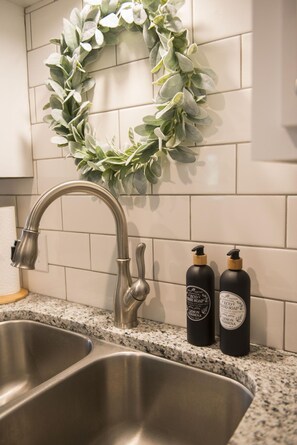 A kitchen with a stainless steel sink, a faucet, and two bottles of soap on the counter.