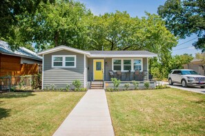 A single-story house with a front porch, a yellow door, and a driveway leading to a parked SUV.