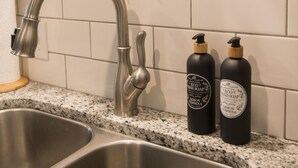 Eine Küche mit einer Edelstahl-Spüle, einem silbernen Wasserhahn und zwei Flaschen umweltfreundlicher Handseife.