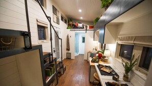 A compact kitchen with wooden flooring, a dining area with a table and chairs, and a small seating area with cushions. - Montana Escape Tiny House in Waco 12 min to Magnolia and Baylor (Waco)