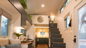 A modern interior with a wooden floor, a staircase, a kitchen area, and a seating area with a bench and cushions. - Montana Escape Tiny House in Waco 12 min to Magnolia and Baylor (Waco)