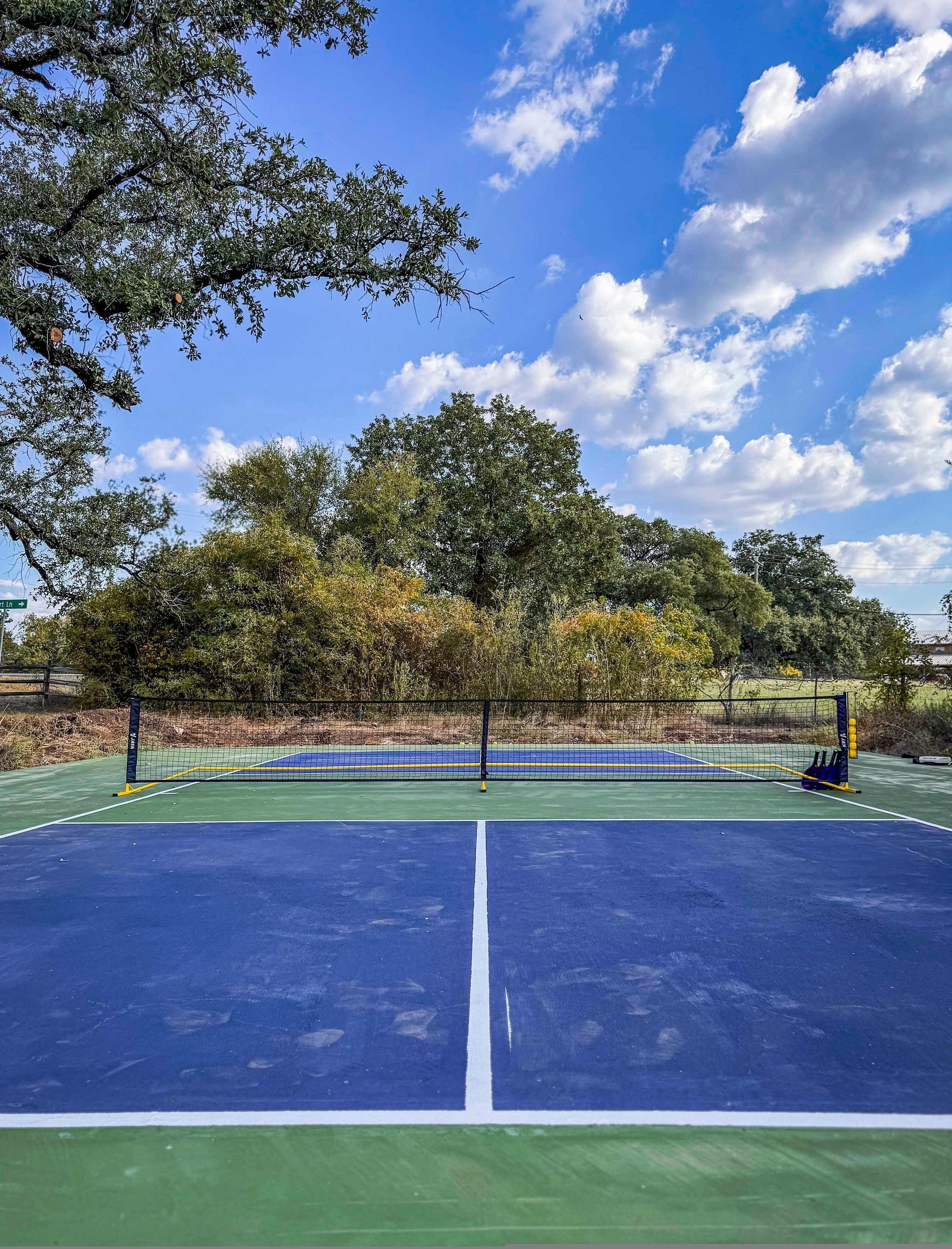 Een buitenbaan voor tennis met een net, omringd door bomen en een heldere lucht.