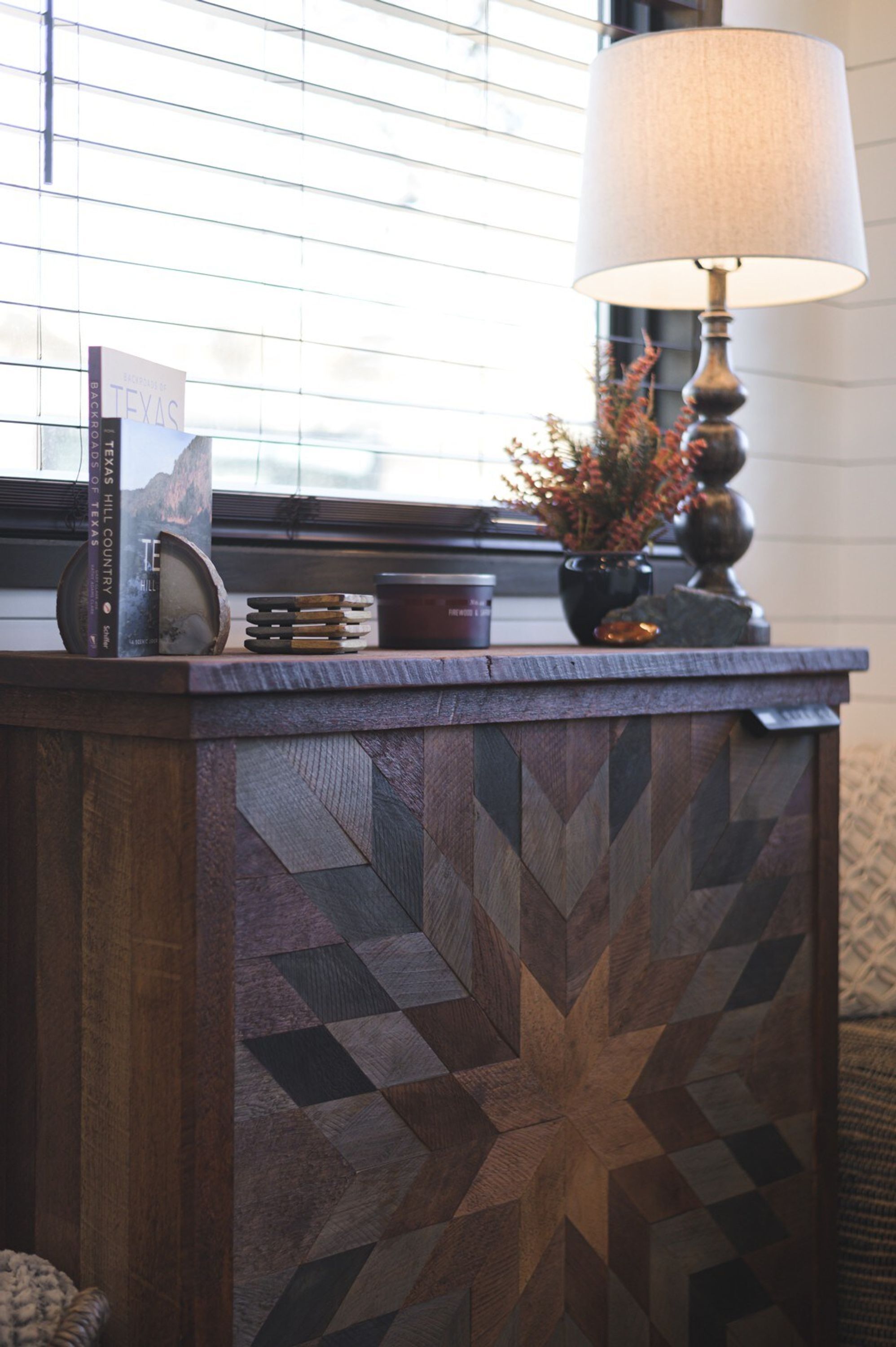 A wooden counter with a geometric pattern, a lamp, books, and a vase with flowers.