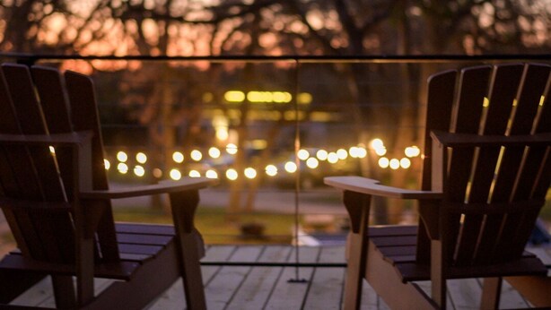 Deux fauteuils Adirondack en bois, placés sur une terrasse en bois, avec des guirlandes lumineuses en arrière-plan.