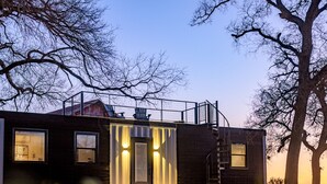 Un bâtiment moderne à l’extérieur sombre, doté de grandes fenêtres et d’un escalier apparent menant à un balcon.